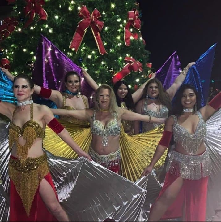 Dancers with gold Isis wings in front of a Christmas tree